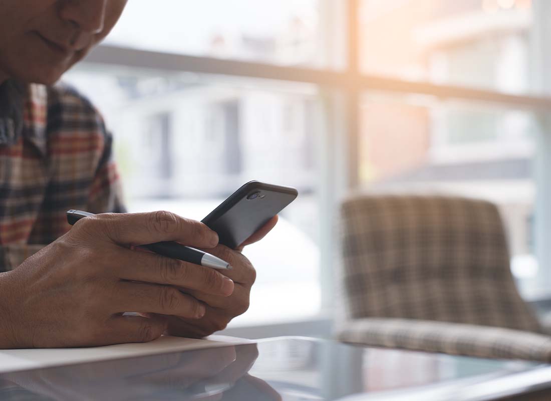 Health Savings Account - Close-up of a Man in a Flannel Shirt Using His Smart Phone and Laptop in a Cafe to Pay for Medical Expenses